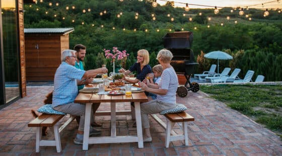 Family surrounding a table in a backyard patio space, atop a patterned brick-layed patio